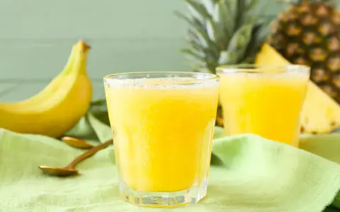 Orzeźwiający koktajl z ananasa i banana, idealny na upalne dni. Obok leżą świeże owoce i złote łyżeczki.