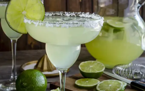 Spicy Margarita przepis: orzeźwiający drink z solą na brzegu kieliszka, limonkami i dzbankiem pełnym zielonego napoju.