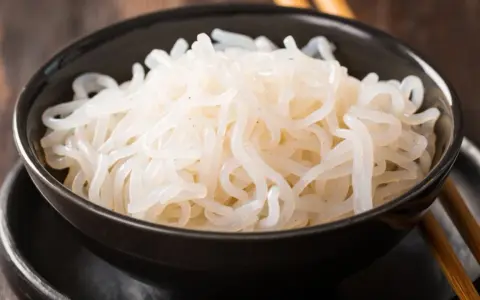 Misternie ułożony makaron konjac w czarnej misce, gotowy do spożycia z pałeczkami.