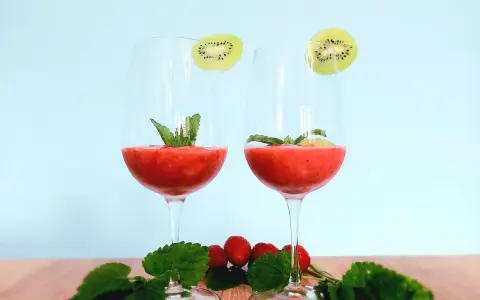Dwa kieliszki orzeźwiającego drinka truskawkowego z rumem, ozdobione plasterkami kiwi i miętą. Na drewnianym blacie leżą świeże truskawki i listki mięty.