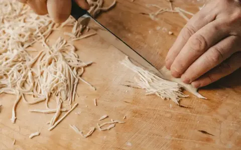 Ręcznie krojenie makaronu do rosołu na drewnianej desce. Drobne nitki ciasta powstają pod ostrzem noża.