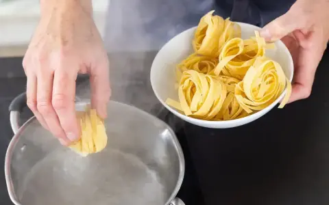 Ręka wkłada tagliatelle do wrzącej wody. Kluczowe jest, na jakim ogniu gotować makaron, by był al dente.