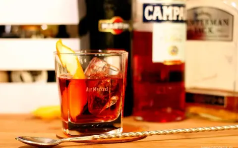 Klasyczny drink z pomarańczą i lodem. Wybór między Negroni czy Boulevardier? Na stole widać butelki Martini, Campari i Jack Daniel's.