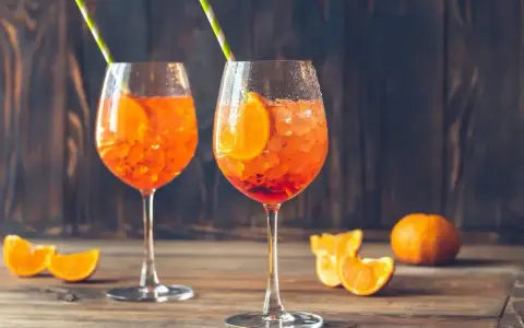 Dwa orzeźwiające drinki z aperolem, ozdobione plastrami pomarańczy i słomkami, na drewnianym blacie.
