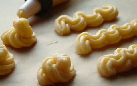 Kremowe eklery z czekoladą i profiteroles w trakcie przygotowania. Widać rękaw cukierniczy i wyciskane ciasto.