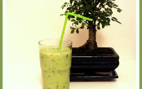 Orzeźwiający koktajl z kiwi i banana, z zieloną słomką, obok miniaturowego drzewka bonsai.