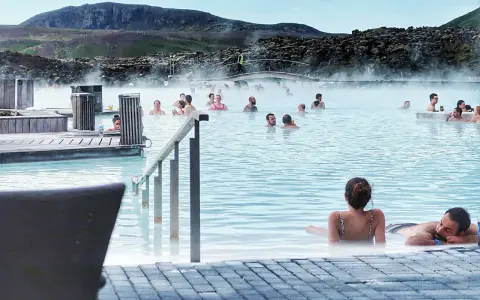 Relaks w Blue Lagoon, geotermalnym basenie z parą unoszącą się nad turkusową wodą. Ludzie kąpią się i odpoczywają.