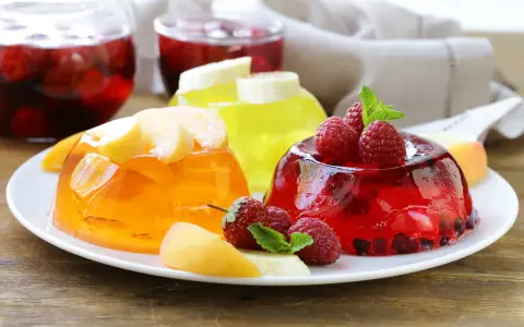 Kolorowe galaretki z owocami: pomarańczowa z brzoskwiniami, żółta z bananem, czerwona z malinami i porzeczkami. Idealne, gdy dodać owoce do galaretki, by była pyszna.