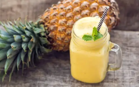 Orzeźwiający koktajl z ananasa i banana, ozdobiony miętą, na drewnianym tle.