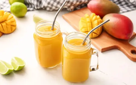 Orzeźwiający drink z wódką mango, podany w słoiczkach z metalowymi słomkami, obok świeżych owoców mango i limonek.