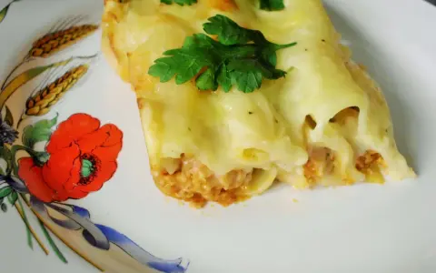Cannelloni z mięsem i beszamelem przepis. Pyszne danie zapieczone pod beszamelem, udekorowane natką pietruszki, na talerzu z makami.