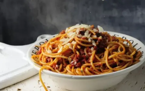 Gorące spaghetti z sosem bolońskim i parmezanem, parujące w misce. Czy to bucatini czy spaghetti, smakuje wyśmienicie!