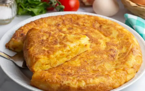 Złocista tortilla ziemniaczana, idealna na szybki obiad z niczego. Na talerzu, obok pomidorów i jajek.