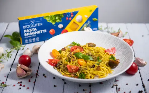 Pyszny talerz makaronu spaghetti bezglutenowego z pesto, pomidorkami i migdałami. Obok pudełko makaronu.