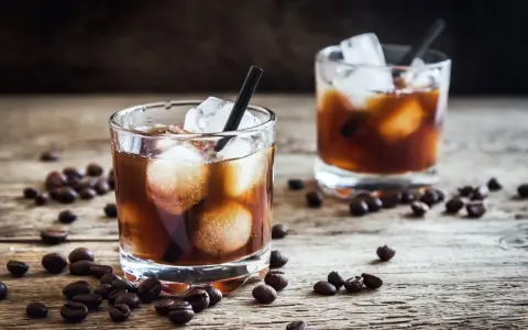 Dwa szklanki z lodem i ciemnym napojem, otoczone ziarnami kawy. Idealny czarny rusek drink na drewnianym blacie.