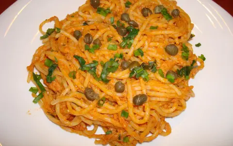 Pyszne spaghetti z tuńczykiem i kaparami, posypane szczypiorkiem, na białym talerzu.