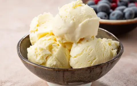 Pyszne, kremowe lody waniliowe w miseczce. Idealne na deser, gdy szukasz prostego przepisu na lody. W tle miska z jagodami i malinami.
