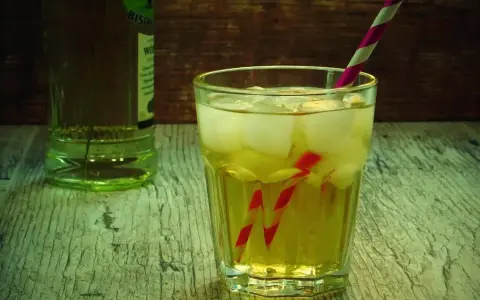 Orzeźwiający drink z lodem i słomką, idealny do przygotowania według przepisu na French Martini. Obok butelka alkoholu.