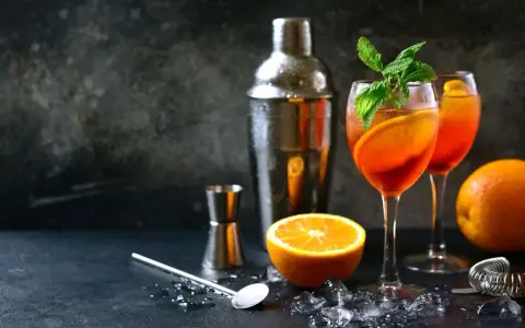 Orzeźwiający aperol z szampanem, udekorowany pomarańczą i miętą, gotowy do podania. Obok shaker i akcesoria barmańskie.