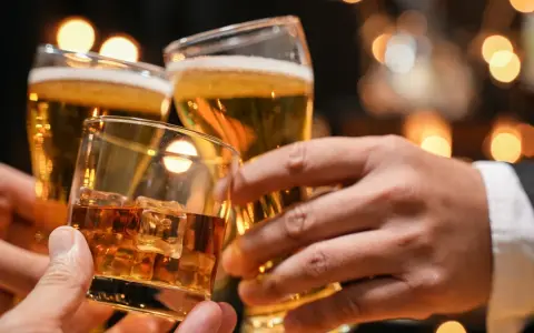 Trzy dłonie wznoszą toast: jedna z whisky na lodzie, dwie z piwem. Lepiej 2 drinki czy 2 piwa?