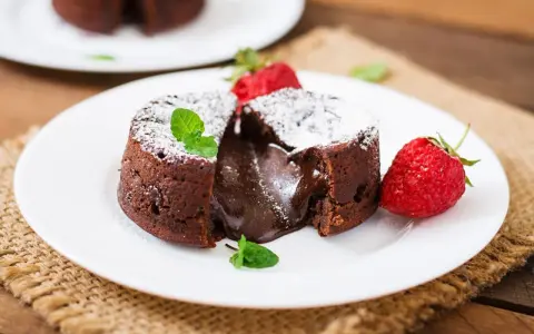 Pyszny fondant czekoladowy z płynnym środkiem, przypominający małe soufflé czekoladowe, podany z truskawkami i miętą.