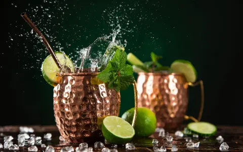 Dwa miedziane kubki z Moscow Mule i London Mule, ozdobione limonką i miętą, z bryzgami wody i lodem.