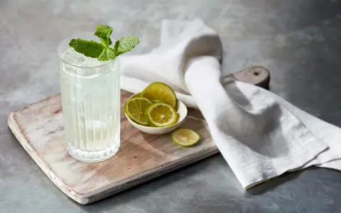 Orzeźwiający mojito z ginem, udekorowany miętą i podany z plasterkami limonki na drewnianej desce.