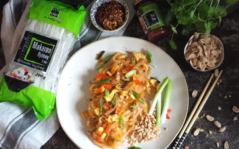 Gotowy Pad Thai przepis na talerzu, obok makaron ryżowy, orzeszki ziemne i sos.