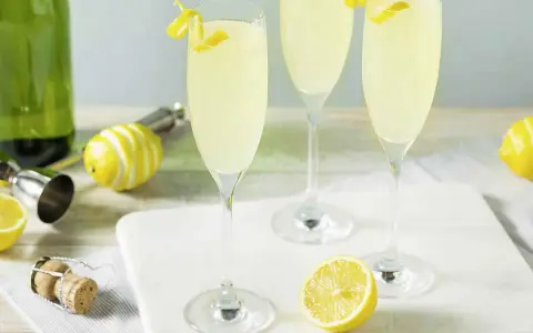 Trzy kieliszki musującego drinka French 75, jeden na ginie, drugi na koniaku, z cytrynową dekoracją.
