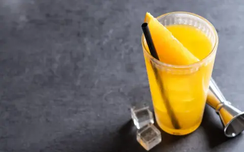 Orzeźwiający drink z wódką i sokiem pomarańczowym, ozdobiony plasterkiem pomarańczy, z kostkami lodu i miarką barmańską obok.