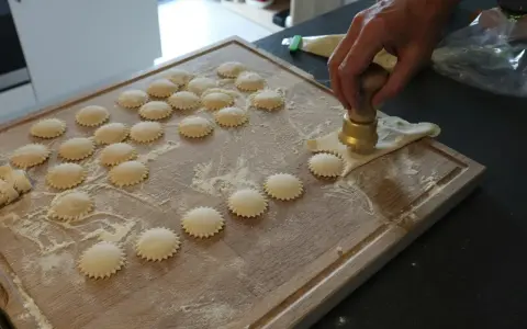 Ravioli z ricottą i szpinakiem przepis: ręcznie robione pierożki na desce, posypane mąką.