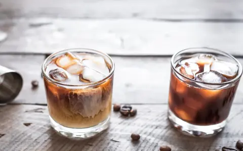 Dwa drinki na drewnianym blacie: jeden to White Russian, drugi to Black Russian.