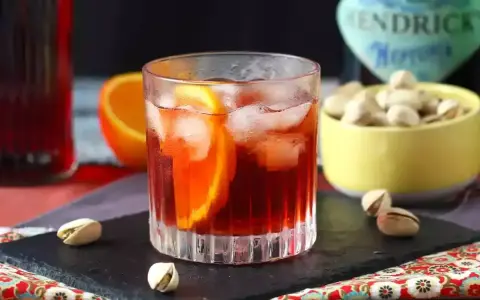 Przepis na Negroni Sbagliato: orzeźwiający drink z pomarańczą i lodem, obok miseczka pistacji.
