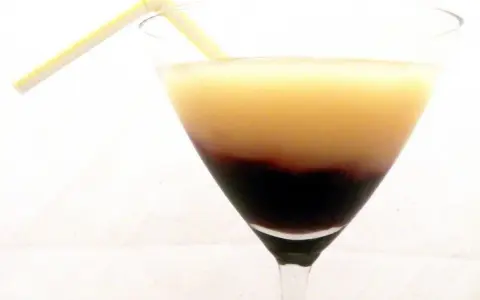Dwukolorowy drink w kieliszku, z warstwą soku z czarnej porzeczki na dnie i jasnym płynem na górze, ozdobiony żółtą słomką.