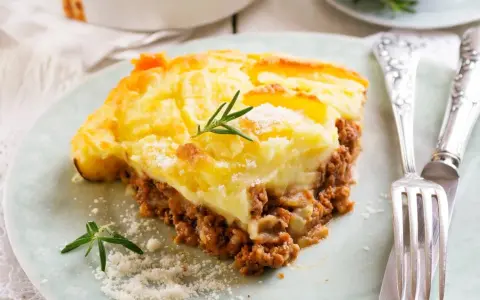 Pyszna zapiekanka pasterska (Shepherd's Pie) z warstwą mielonego mięsa i kremowym purée ziemniaczanym, ozdobiona gałązką rozmarynu.