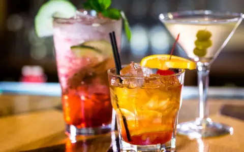 Kolorowe drinki z wódką smakową: czerwony z ogórkiem i miętą, bursztynowy z pomarańczą i wiśnią, oraz martini z oliwkami.
