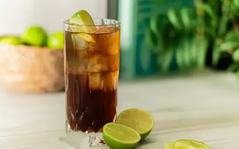 Orzeźwiający Cuba Libre, czyli rum z colą i limonką, z kostkami lodu i świeżymi limonkami w tle. Idealny na upalne dni.
