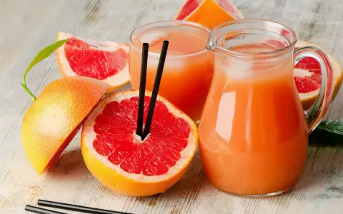 Orzeźwiający drink z grejpfrutem, podany w dzbanku i szklance, otoczony świeżymi owocami. Idealny na upalne dni.