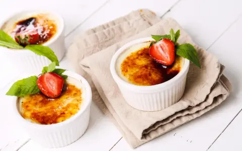 Trzy kremowe desery, Crème brûlée czy crema catalana, ozdobione truskawkami i miętą, kuszą skarmelizowanym cukrem.