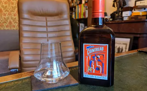 Cointreau kontra Triple Sec w koktajlach: butelka Cointreau i pusty kieliszek na biurku.