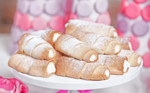 Domowe rurki z kremem, posypane cukrem pudrem, wyglądają apetycznie obok pastelowych dekoracji.