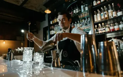 Barman przygotowuje drinki, pokazując, jak założyć drink bar. Na półkach stoją butelki alkoholi.