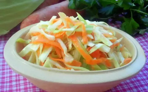 Świeża surówka z kapusty i marchewki, jak z chińskiej restauracji, w miseczce na kratkowanym obrusie.