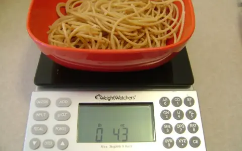 Ugotowany makaron w czerwonej misce na wadze cyfrowej pokazującej 0.43 funta.