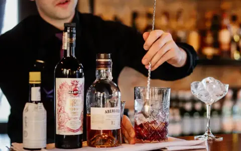 Barman miesza składniki, przygotowując najlepszy drink z whisky. Na blacie butelki Aberlour, Martini i inne.
