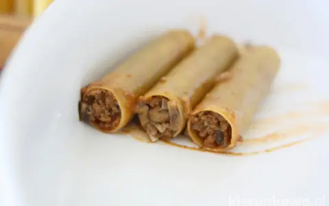 Trzy cannoloni z farszem mięsnym, wyglądające jak naleśniki z mięsem, leżą na białym talerzu.