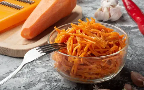 Pyszna surówka z marchewki jak z restauracji, gotowa do podania. Obok marchewka, tarka, czosnek i papryczka chili.
