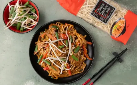 Gotowy **Chow Mein przepis** na talerzu: makaron z warzywami i kiełkami fasoli, obok paczka makaronu i miseczka kiełków.