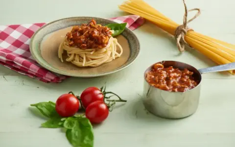 Pyszne spaghetti z sosem bolońskim, przygotowane z pomocą przyprawy do spaghetti Knorr. Obok świeże pomidory i bazylia.