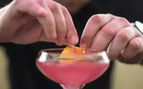 Ręce dekorują drinka skórką pomarańczy. To ostatni krok w przygotowaniu Cosmopolitan przepis.